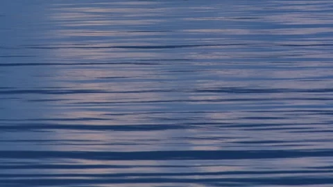 A close-up of the yellowish-orange moon's reflection on a calm blue sea in the Stock Footage 342283158