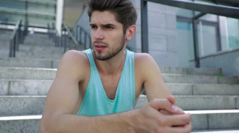 Close-up of young attractive man model sitting at stadium stairs after training Stock Footage 65380591