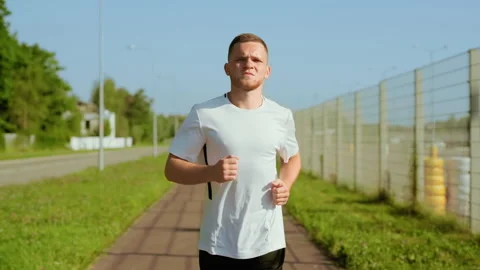Close up young attractive man running on street at sunlight. Runner jogging Stock Footage 140365818