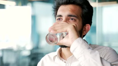 Close up A young bearded man in a shirt drinks water from a glass while sitting  Stock Footage 248606056