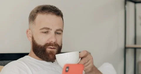 Close up of young bearded man using his smartphone and smiling while drinking Stock Footage 127151993