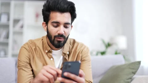Close up. Young bearded man using smartphone sitting on sofa in living room  Stock Footage 252201703