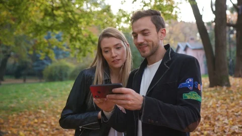Close up young beautiful couple stand talk use phone in park lifestyle love male Stock Footage 102740997