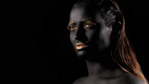Close-up of a young beautiful woman's face with black and gold paint on her skin Stock Footage 144433707