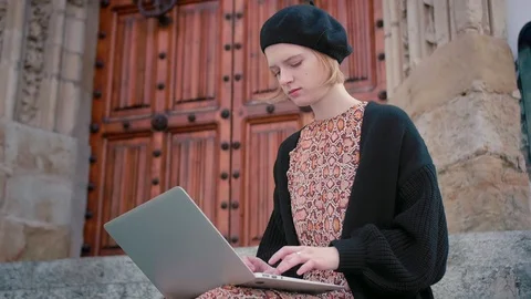 Close up of young blond trendy looking journalist girl in beret siting on stair Stock Footage 105059268