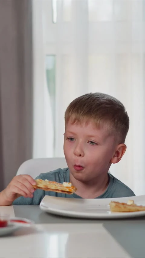 Close up young boy bringing pizza slice to mouth while seated at table indoors Stock Footage 344789654
