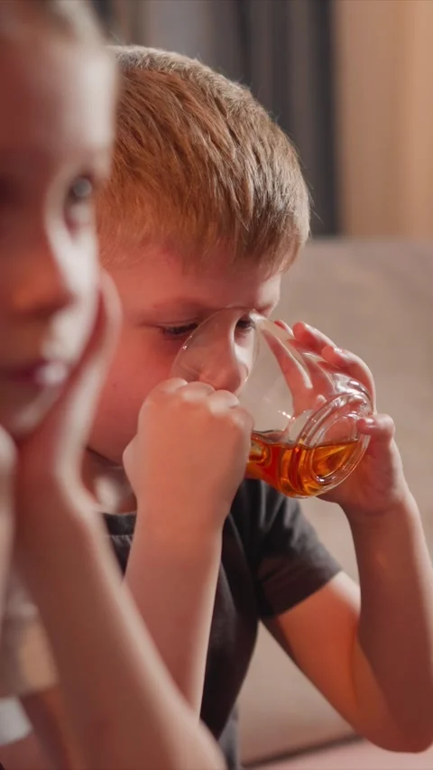 Close up of young boy drinking golden liquid with another visible nearby in soft Stock Footage 344789871