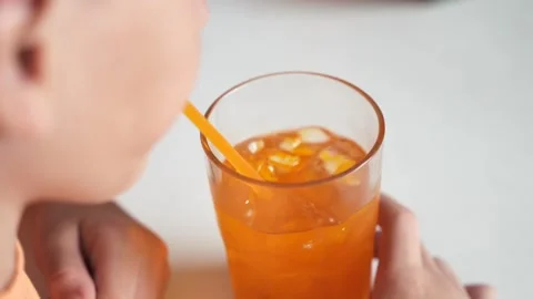 Close up of young boy drinking orange iced soda juice from glass with the straw Stock Footage 279819401