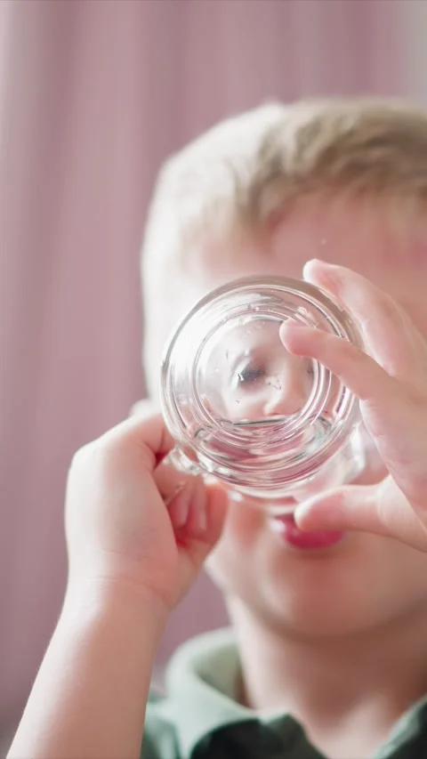 Close up of young boy drinking water from clear glass in soft indoor lighting Stock Footage 344792755