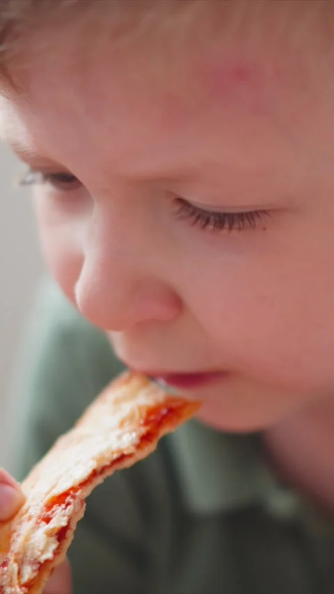 Close up young boy eating pizza slice with cheese and tomato sauce featuring Stock Footage 344794628