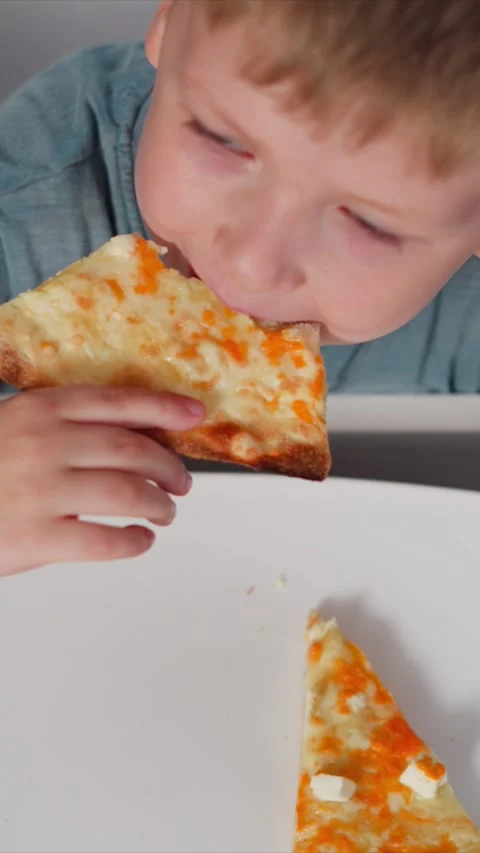 Close up of young boy enjoying cheese pizza with visible hand holding slice on Stock Footage 344794650