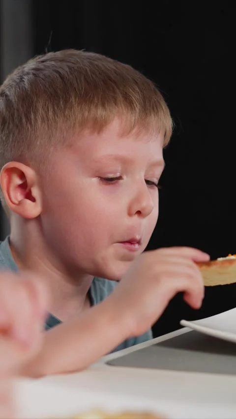 Close up of young boy enjoying cheese pizza slice at table with dark backdrop Stock Footage 344796945