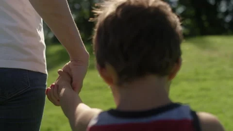 Close-up of a young boy hold his mom's hands as they walk through the park 스톡 동영상 143620717