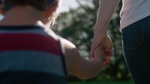 Close-up of a young boy holding his mother's hands while walking through a park 스톡 동영상 143630135