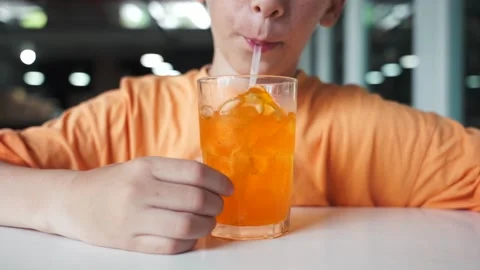 Close up of young boy in orange t shirt blowing bubbles with straw in glass with Stock Footage 279127852