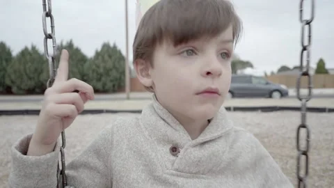 Close up of young boy on swing set wearing paper crown, wild imagination. Video stock 169734543