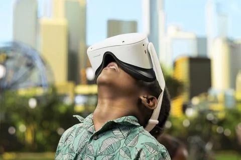 Close up of young boy using VR glasses and raised controllers in city park Stock Photos