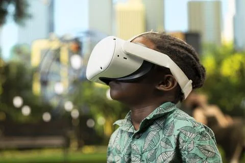 Close up of young boy using VR glasses and raised controllers in city park Stock Photos