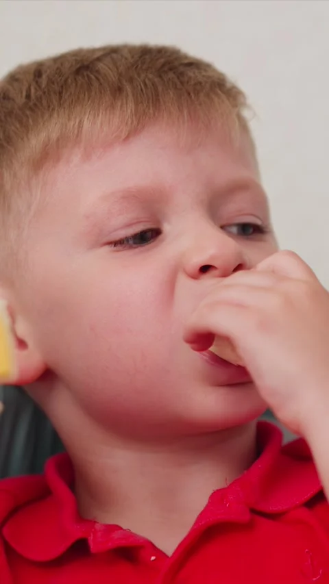 Close up of young boy wearing red poloshirt eating peeled banana with soft Stock Footage 344790663