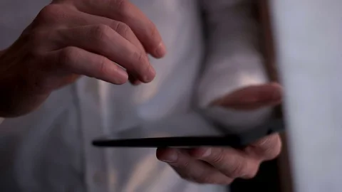 Close up young businessman using tablet computer while standing near window on Stock Footage 75547967