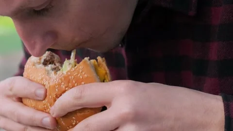 Close up of young Caucasian man eats meat burger in fast food restaurant Stock Footage 236632363
