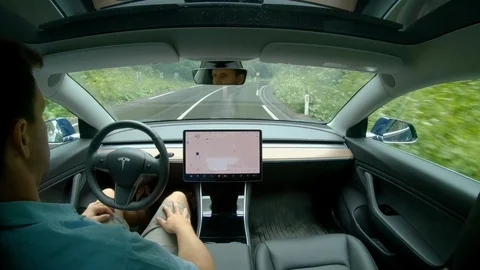 CLOSE UP: Young Caucasian man lets the autonomous car drive him down wet road. Stock Footage 114668498