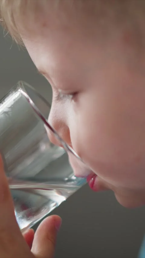 Close up of young child drinking water from clear glass with soft lighting and Stock Footage 344794680