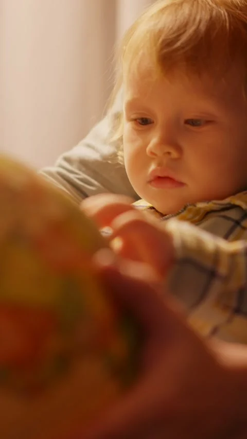 A close-up of a young child with light blonde hair, deeply focused on a globe Stock Footage 307248521