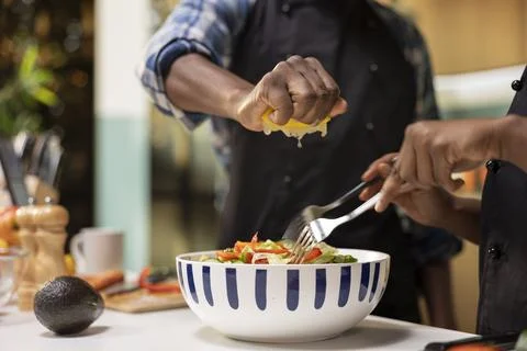 Close up of young couple adding lemon juice over salad and mixing veggies Fotos Stock
