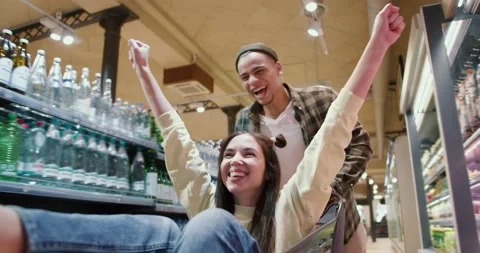 Close up of a young couple having fun, man pushing shopping cart with his Stock Footage 235347609