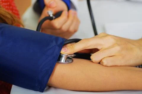 Close up of a young doctor using the stethoscope to hear the pulse while a woman 스톡 사진