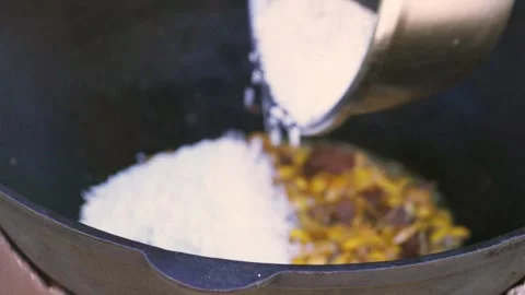 Close-up of young female chef adding rice into large kazan for pilaf Stock Footage 333038646