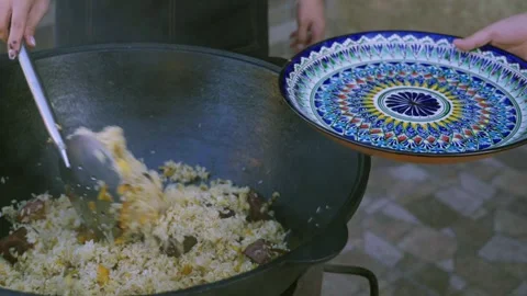 Close-up of young female cook serving Uzbek plov from large cauldron onto Stock Footage 333040670