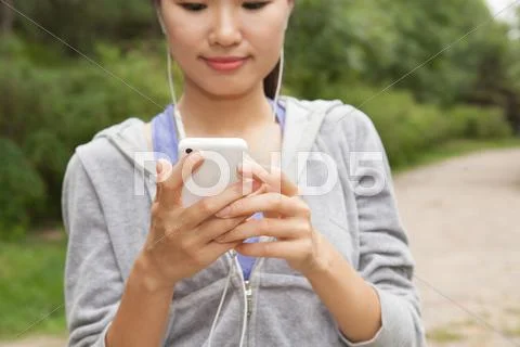 Close Up Of Young Female Runner Selecting Music From Smartphone In Park