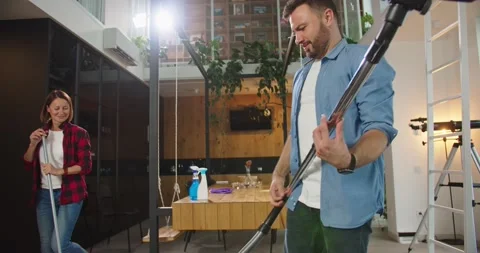 Close up of young funny couple having fun, dancing, singing using mop and vacuum Stock Footage 141108596
