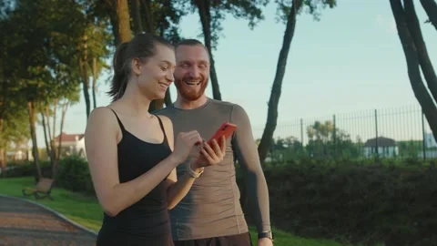 Close up young funny man and woman use phone smiling after morning run watching Stock Footage 138645894