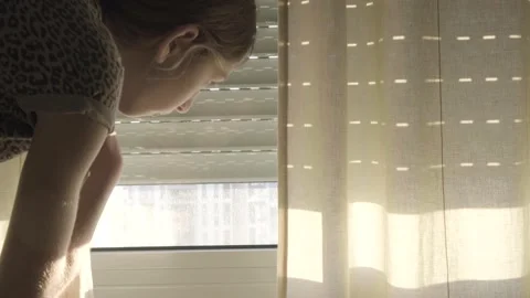 Close up of young girl moving the window blinds and peeking through to the Vidéo 148999930