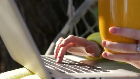 Close up of young girl using laptop and drinking tea or coffee on rope swing in Stock Footage 221014599