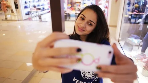 Close up young girl using smartphone taking selfie smile in shopping mall poses Stock Footage 99254293