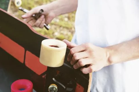 A close-up of a young guy changes his wheels on his longboard and adjusts the Stock Photos