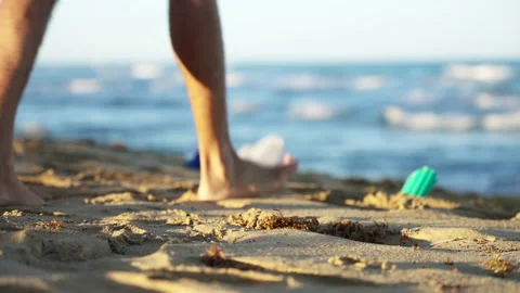 Close-up of a young guy collecting plastic trash on a sandy beach Stock Footage 169451237