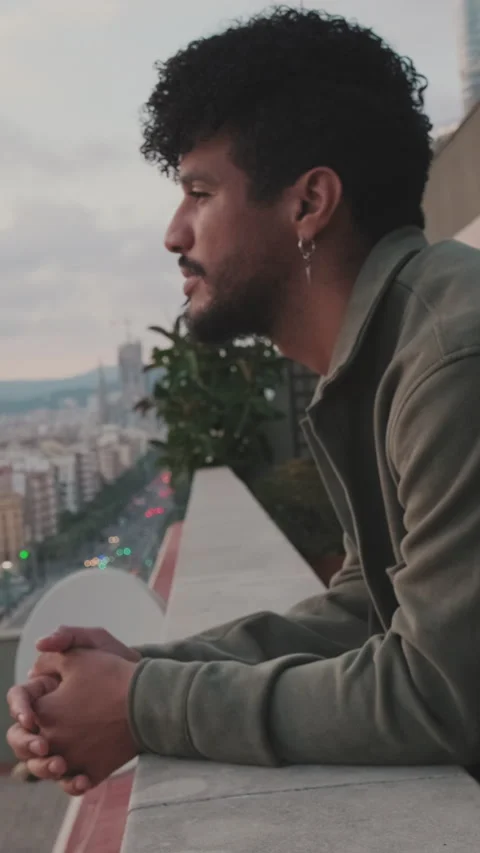 Close-up of young guy is standing on the balcony looking at the city Stock Footage 250840160