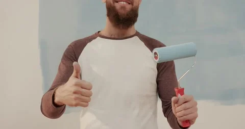 Close up of young handsome caucasian man with beard holding paint roller and Stock Footage 147060016