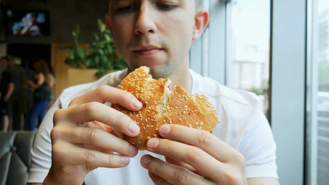 Close-up of young hungry man eats hamburger in a cafe, fast food restaurant Stock Footage 110594274