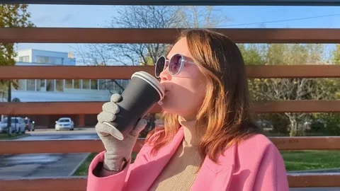 Close up of young lady in a pin coat walking, holding paper cup with coffee by Stock Footage 252439313