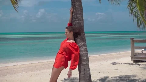 Close up of young lady in red stood in background of sky and blue ocean leaning Stock Footage 276604952