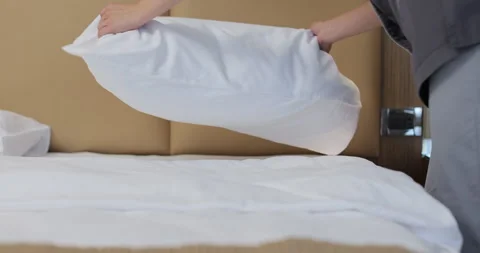 Close-up of young maid in uniform, fluffing pillows and punching them into shape Stock Footage 313993787