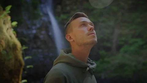 Close up of young males face looking around in forest, waterfall in background Stock Footage 220301704