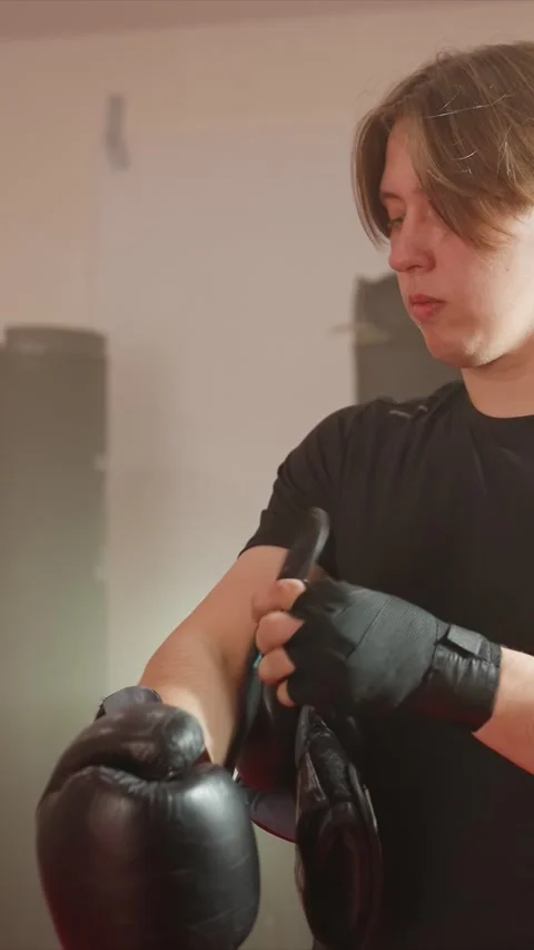 Close up of young man adjusting boxing gloves and wraps in indoor gym with Stock Footage 343094092