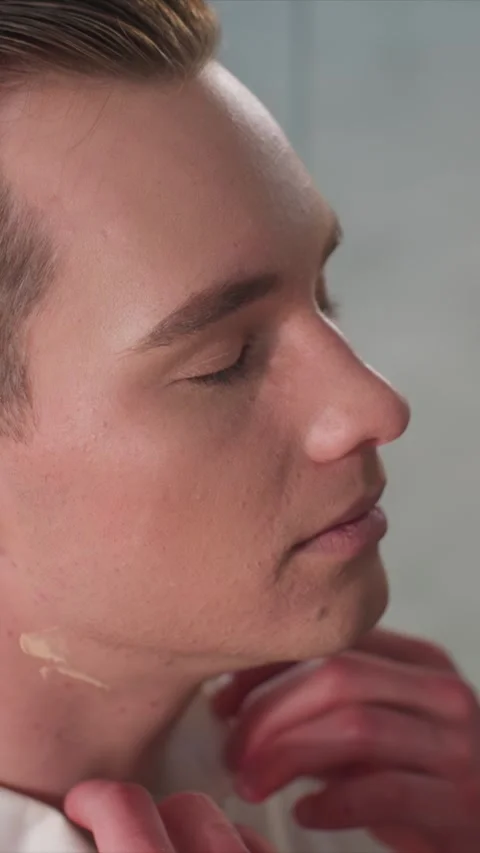 Close up of young man applying cream to neck and ears with hand holding product Stock Footage 344413474